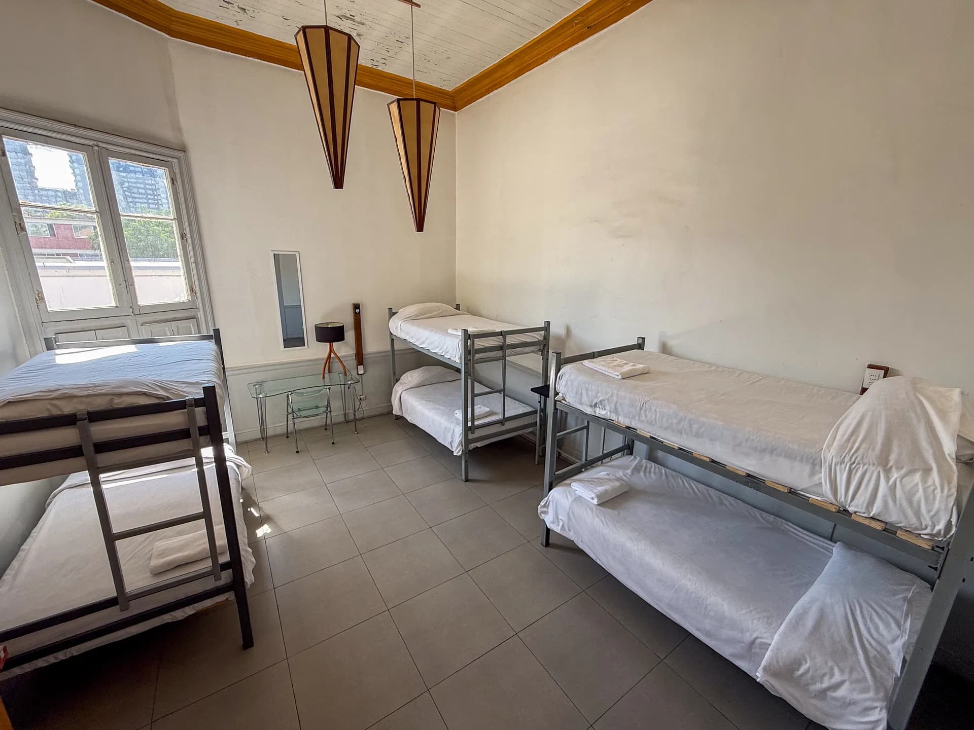 Shared dormitory room at Happy Hostel Santiago with bunk beds, personal lockers and high ceilings with art deco lamps